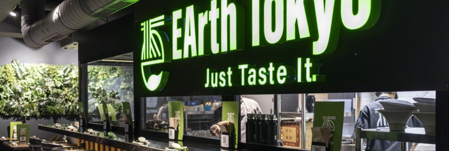 Restaurant mit gr&uuml;nem Leuchtschild 'EArth Tokyo' und dem Slogan 'Just Taste It'. Moderne Einrichtung mit Pflanzenwand., &copy; SMG, Sarah Schmid