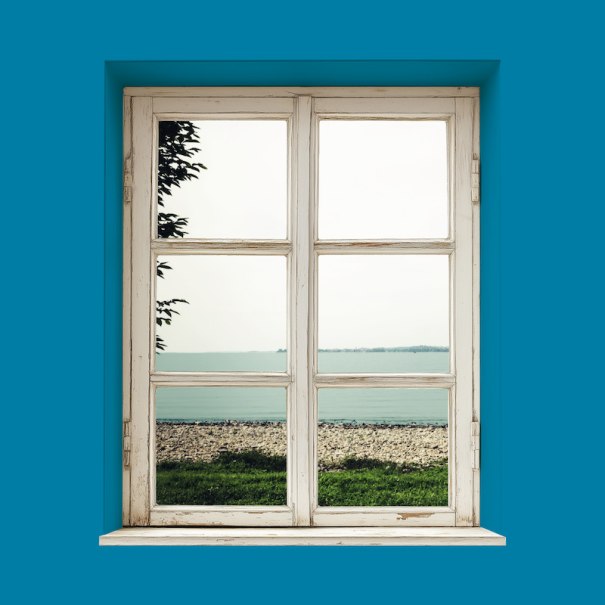 Ein Fenster in einer blauen Wand zeigt einen Strand und das Meer. Der Himmel ist bewölkt, und ein Baum ist am Rand sichtbar., © Theater der Altstadt