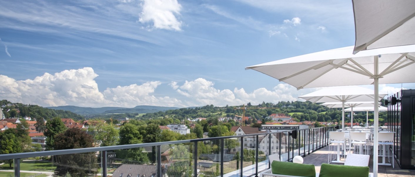 Rooftop bar with white parasols and green cushions, view of a cityscape with hills in the background., © Hotel am Remspark Rooftop bar with white parasols and green cushions, view of a cityscape with hills in the background., © Hotel am Remspark