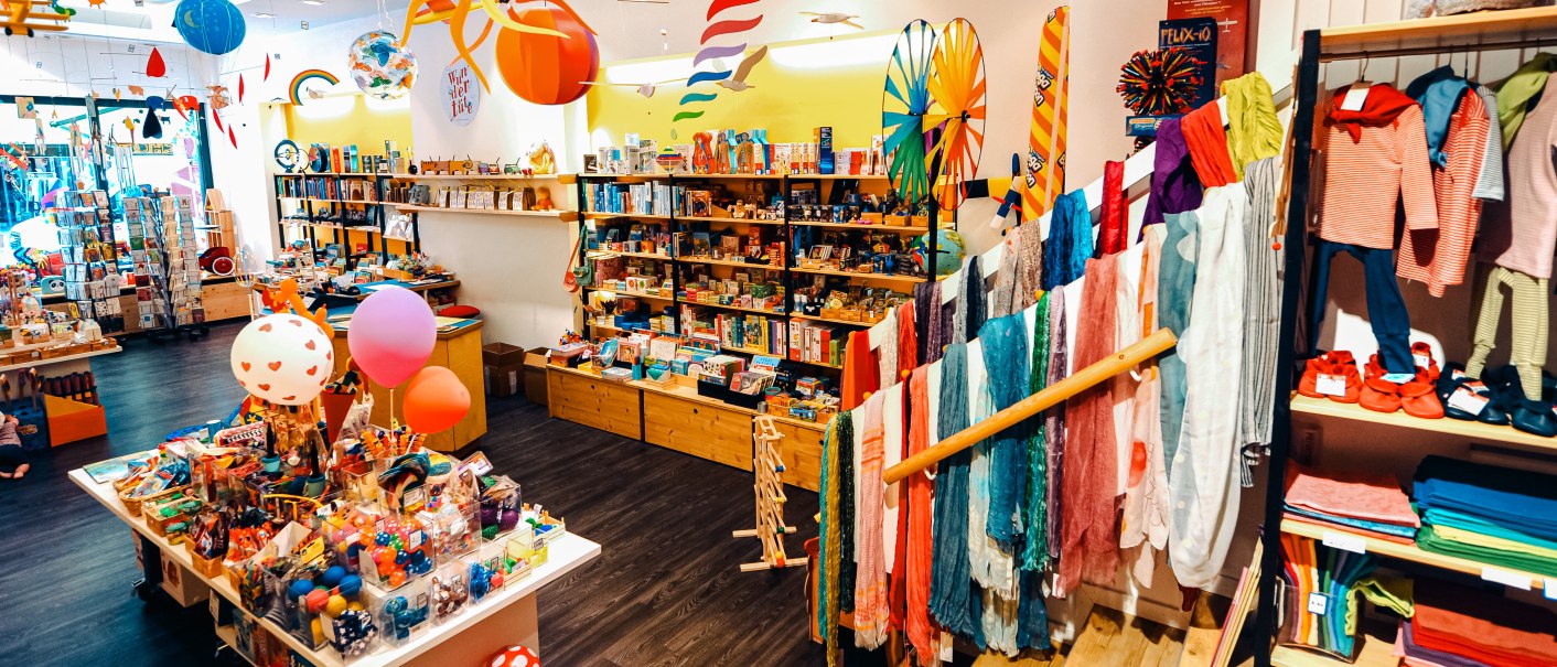 A colorful toy store with shelves full of toys, clothes and decorations. Colorful scarves and toys are prominently displayed., © 1000schön