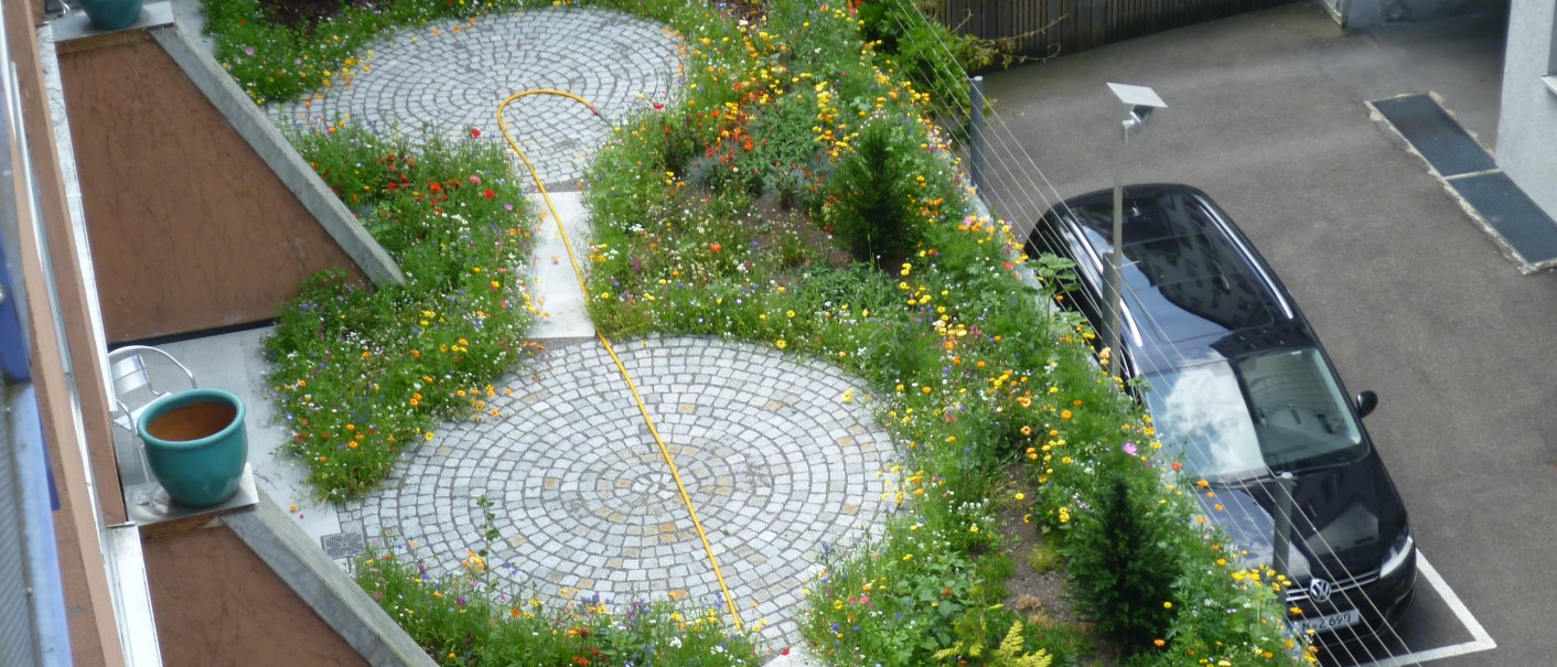 Terrasse mit Blumenbeeten und gepflastertem Weg, daneben ein geparktes Auto. Blick von oben., © Abalon Hotel Ideal Terrasse mit Blumenbeeten und gepflastertem Weg, daneben ein geparktes Auto. Blick von oben., © Abalon Hotel Ideal
