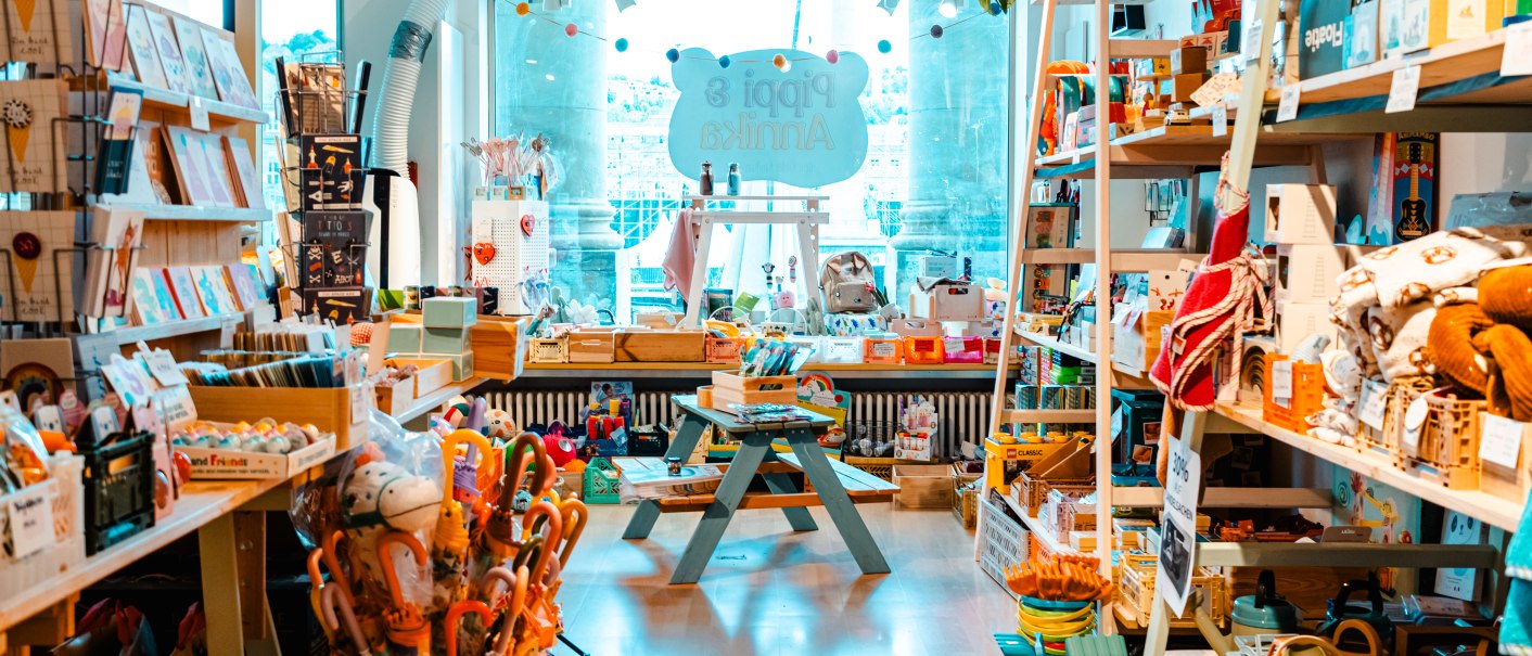 Bunter Spielzeugladen mit Regalen voller Spielsachen, Büchern und Accessoires. Ein Tisch steht in der Mitte, das Schild "Pippi & Annika" im Hintergrund., © SMG_Sarah Schmid