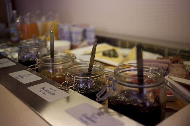 Ein Frühstücksbuffet mit verschiedenen Marmeladengläsern, Getränken und Joghurtbechern im Hintergrund., © AKZENT Hotel Torgauer Hof