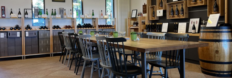 Wine bar with wooden table and chairs, surrounded by wine racks and decorations. Bright, inviting atmosphere with wine bottles and plants., &copy; Weinfactum Bad Cannstatt