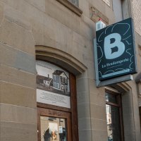 Außenansicht der Bäckerei 'La Boulangerie' mit Schaufenster und Schild. Das Gebäude hat eine steinerne Fassade und spiegelt umliegende Architektur wider., © SMG, Sarah Schmid Außenansicht der Bäckerei 'La Boulangerie' mit Schaufenster und Schild. Das Gebäude hat eine steinerne Fassade und spiegelt umliegende Architektur wider., © SMG, Sarah Schmid