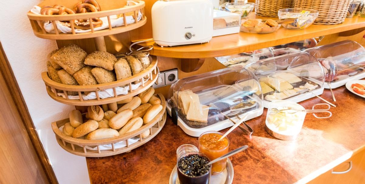 Ein Frühstücksbuffet mit Brötchen, einem Toaster, Marmeladen und Käseplatten. Verschiedene Brotsorten sind in Körben präsentiert., © ARNOTEL GmbH