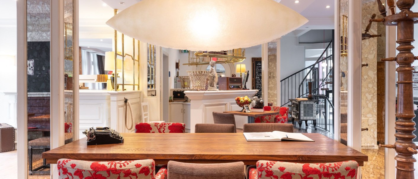 Elegante Lobby mit Holztisch, roten Stühlen und großer Deckenleuchte. Im Hintergrund eine Rezeption und eine Wendeltreppe., © Hotel Weinstadt Elegante Lobby mit Holztisch, roten Stühlen und großer Deckenleuchte. Im Hintergrund eine Rezeption und eine Wendeltreppe., © Hotel Weinstadt