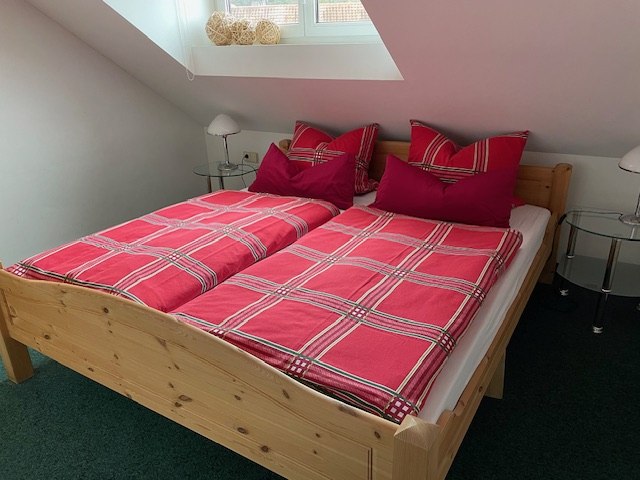 Gemütliches Schlafzimmer mit einem Holzbett, roten karierten Bettbezügen und zwei Nachttischen unter einem Dachfenster., © Weinhof am Württemberg Gemütliches Schlafzimmer mit einem Holzbett, roten karierten Bettbezügen und zwei Nachttischen unter einem Dachfenster., © Weinhof am Württemberg