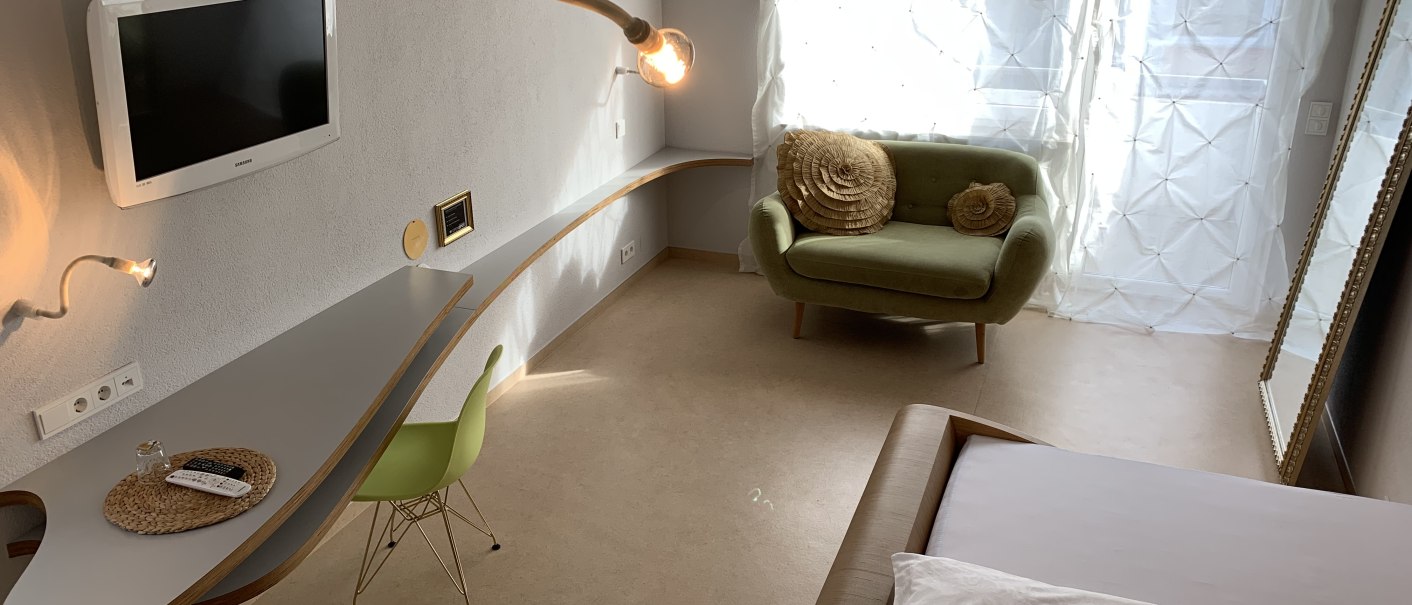Modernes Zimmer mit grünem Sessel, Wand-TV, geschwungenem Schreibtisch und großen Fenstern mit weißen Vorhängen., © TOMAS Modernes Zimmer mit grünem Sessel, Wand-TV, geschwungenem Schreibtisch und großen Fenstern mit weißen Vorhängen., © TOMAS
