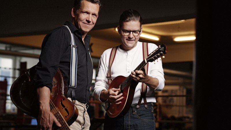 Zwei Männer spielen Gitarren in einem Raum mit gedämpfter Beleuchtung. Beide tragen Hosenträger und wirken konzentriert und zufrieden., © Christian Kaufmann Zwei Männer spielen Gitarren in einem Raum mit gedämpfter Beleuchtung. Beide tragen Hosenträger und wirken konzentriert und zufrieden., © Christian Kaufmann