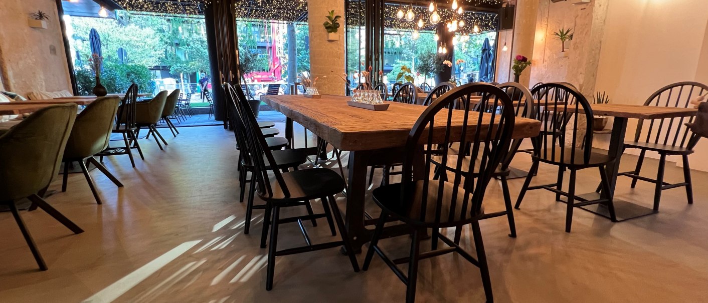 Ein stilvoll eingerichtetes Restaurant mit Holztischen, schwarzen Stühlen und einer Decke voller Lichterketten., © heavenskitchen Ein stilvoll eingerichtetes Restaurant mit Holztischen, schwarzen Stühlen und einer Decke voller Lichterketten., © heavenskitchen