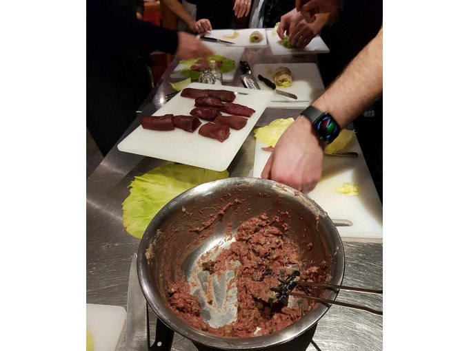 Participants in a cooking course prepare meat and ingredients on chopping boards. A bowl of meat mixture stands in the foreground., © Kultweine-Kochwelten-Kunstücke - Kochschule Sonja Lenz Participants in a cooking course prepare meat and ingredients on chopping boards. A bowl of meat mixture stands in the foreground., © Kultweine-Kochwelten-Kunstücke - Kochschule Sonja Lenz
