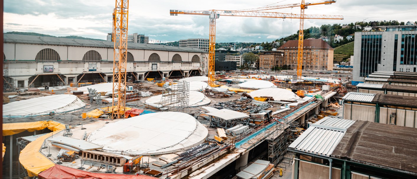 Großbaustelle mit mehreren Kränen, Gebäuden im Hintergrund und abgedeckten Bauflächen. Wolkiger Himmel und städtische Umgebung., © SMG Stuttgart Marketing GmbH - Sarah Schmid