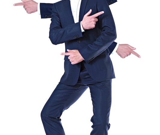 Ein Mann in einem blauen Anzug steht vor weißem Hintergrund. Er hat mehrere Arme, die in verschiedene Richtungen zeigen, was eine humorvolle Pose ergibt., © Rosenau Kultur e.V. Ein Mann in einem blauen Anzug steht vor weißem Hintergrund. Er hat mehrere Arme, die in verschiedene Richtungen zeigen, was eine humorvolle Pose ergibt., © Rosenau Kultur e.V.