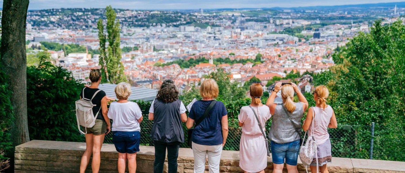 Eine Gruppe von Menschen steht auf einer Plattform und blickt auf eine Stadtlandschaft mit roten Dächern und grünen Hügeln im Hintergrund., © Thomas Niedermüller