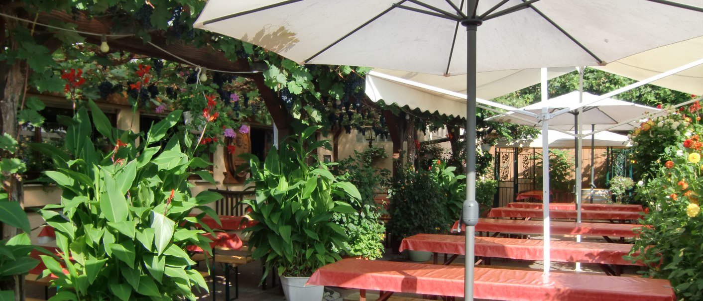 Cozy outdoor area with tables, benches, parasols and lush plants in a broom restaurant., © Simone Mack