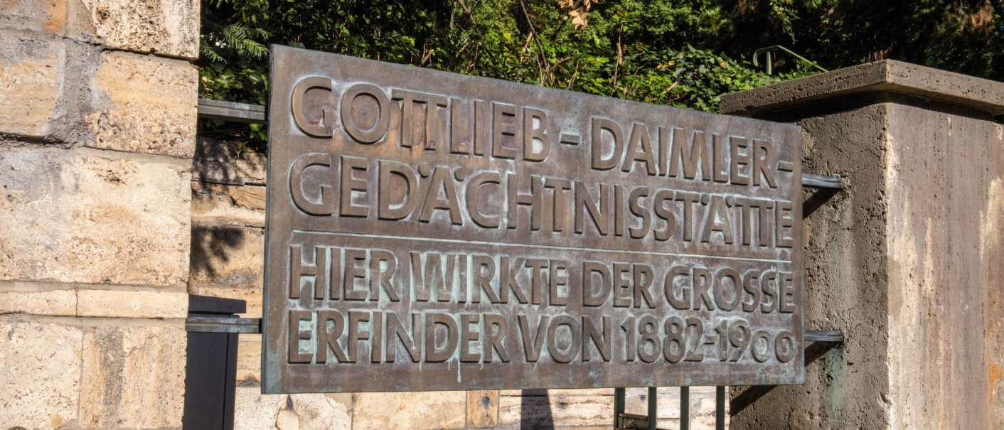 Metal sign on a stone wall with the inscription 'Gottlieb Daimler Memorial Site'. Surrounded by green vegetation., © Stuttgart-Marketing GmbH Achim Mende