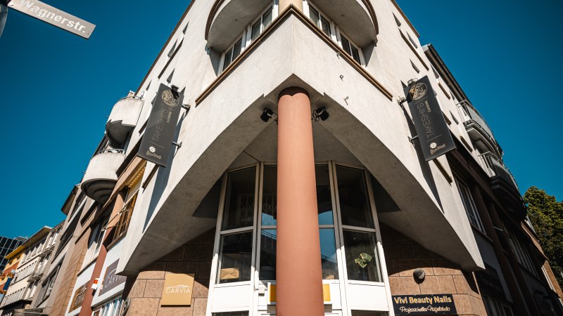 Eckgebäude mit Schildern von Takeshiis Lounge und Vivi Beauty Nails, aufgenommen von unten. Straßenschild Wagnerstraße sichtbar, blauer Himmel im Hintergrund., © SMG Stuttgart Marketing GmbH - Sarah Schmid