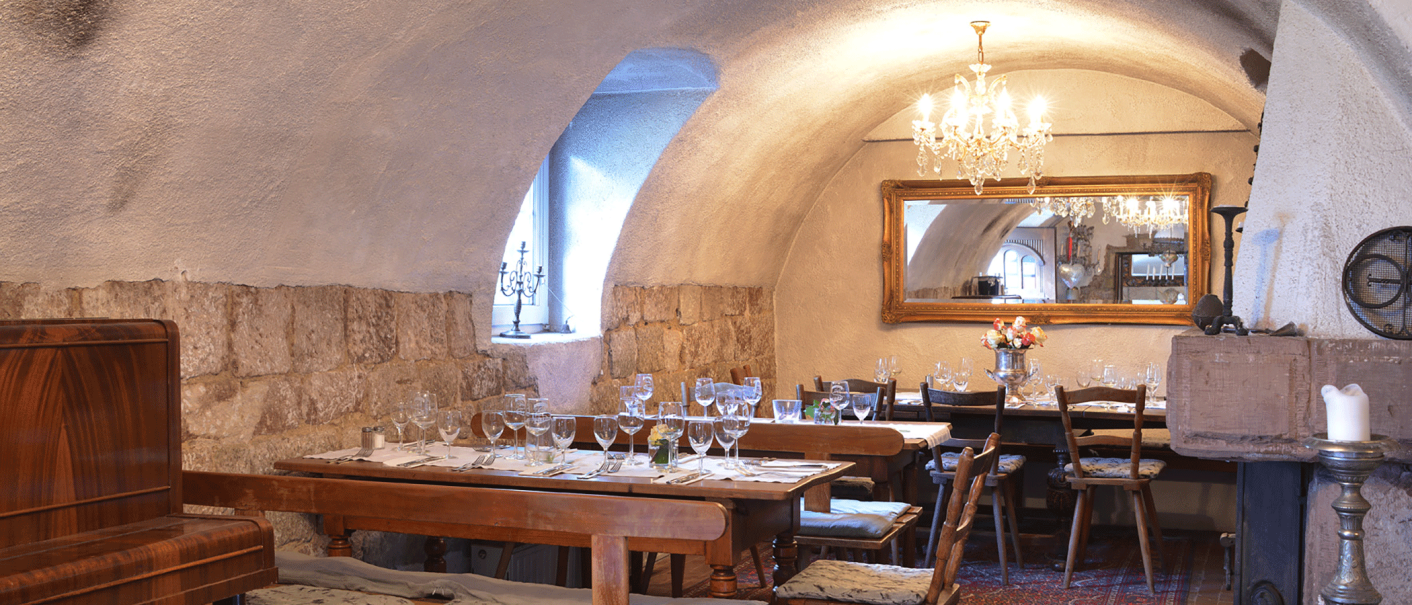 Gemütlicher Gastraum mit gedeckten Holztischen, Kronleuchter, Spiegel und rustikalen Steinwänden. Elegante Atmosphäre mit Kerzen und Blumen., © FreCla Gastronomiebetriebe GmbH Gemütlicher Gastraum mit gedeckten Holztischen, Kronleuchter, Spiegel und rustikalen Steinwänden. Elegante Atmosphäre mit Kerzen und Blumen., © FreCla Gastronomiebetriebe GmbH