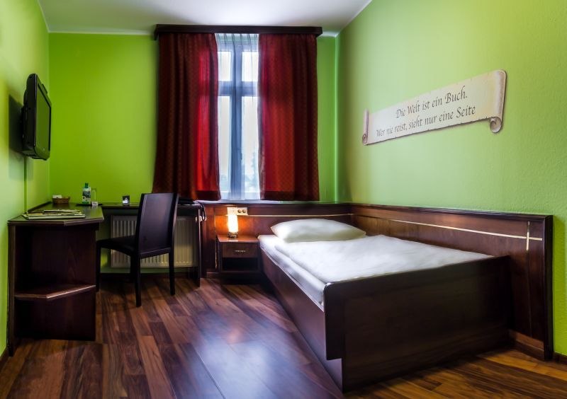 A cozy single room with green-painted walls, a single bed, desk and chair. A red curtain hangs from the window., &copy; TOMAS