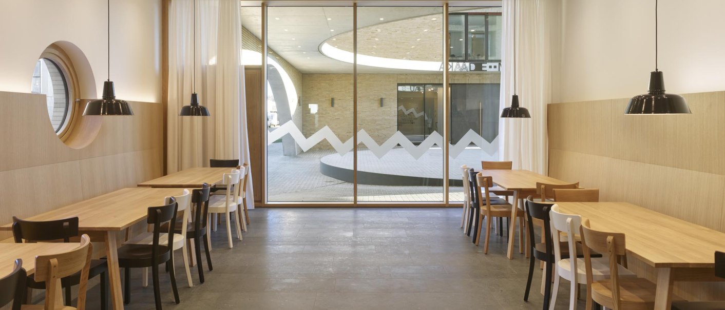 A modern caf&eacute; with wooden tables and chairs, large windows, and hanging lamps. Bright, minimalist decor with a view of the outdoors., &copy; TOMAS