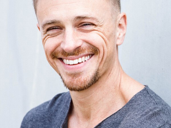 A man with short hair and a beard smiles at the camera. He wears a gray top and stands in front of a gray background., &copy; Rosenau Kultur e.V.