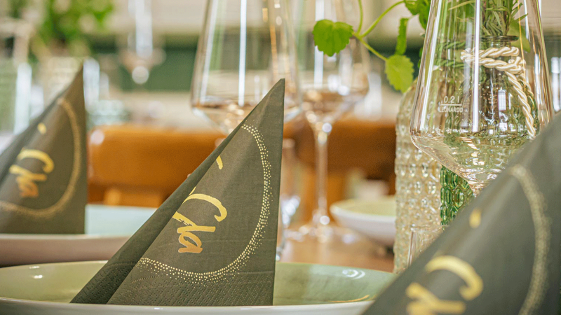 Ein elegant gedeckter Tisch mit gefalteten Servietten, Gläsern und dekorativen Elementen. Die Servietten tragen den Schriftzug 'Cla'., © FreCla Gastronomiebetriebe GmbH Ein elegant gedeckter Tisch mit gefalteten Servietten, Gläsern und dekorativen Elementen. Die Servietten tragen den Schriftzug 'Cla'., © FreCla Gastronomiebetriebe GmbH