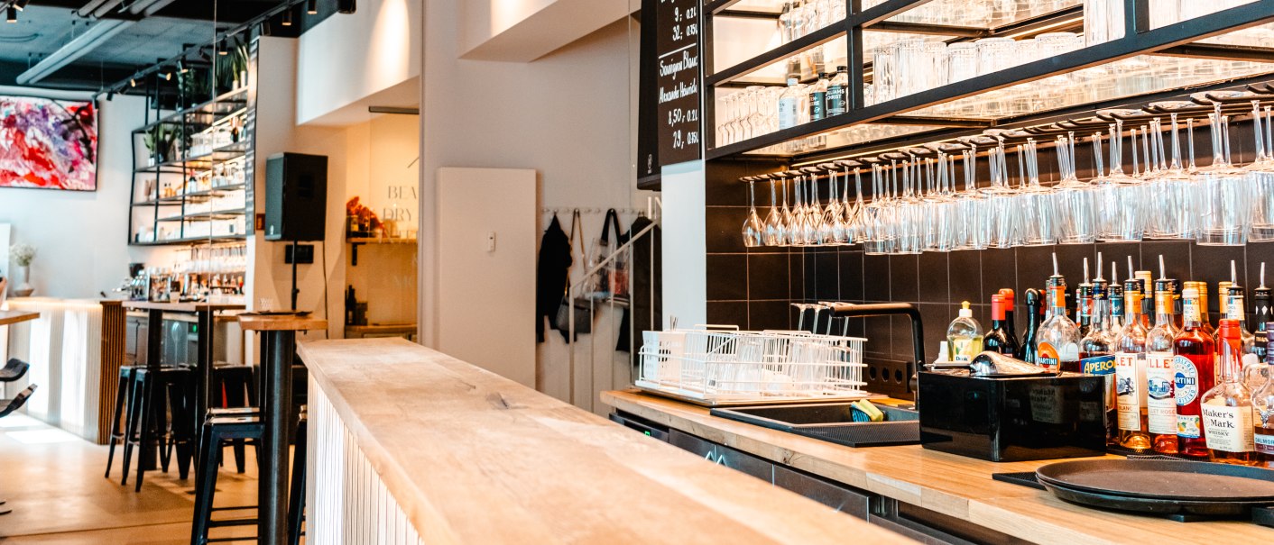 Moderne Bar mit hölzernem Tresen, Regalen voller Gläser und Flaschen. Helle Beleuchtung und stilvolle Einrichtung schaffen eine einladende Atmosphäre., © SMG_Sarah Schmid