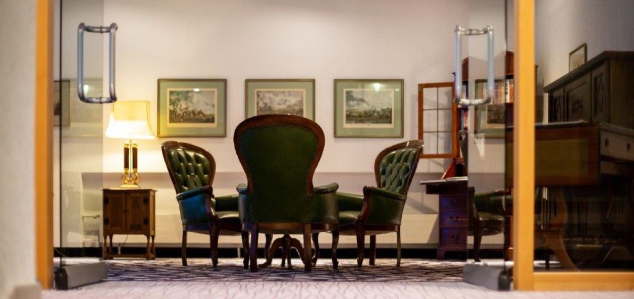Eleganter Raum mit grünen Ledersesseln, Gemälden an der Wand und einer Tischlampe. Holzmöbel und Teppichboden ergänzen das klassische Ambiente., © Kronen Hotel GmbH Eleganter Raum mit grünen Ledersesseln, Gemälden an der Wand und einer Tischlampe. Holzmöbel und Teppichboden ergänzen das klassische Ambiente., © Kronen Hotel GmbH