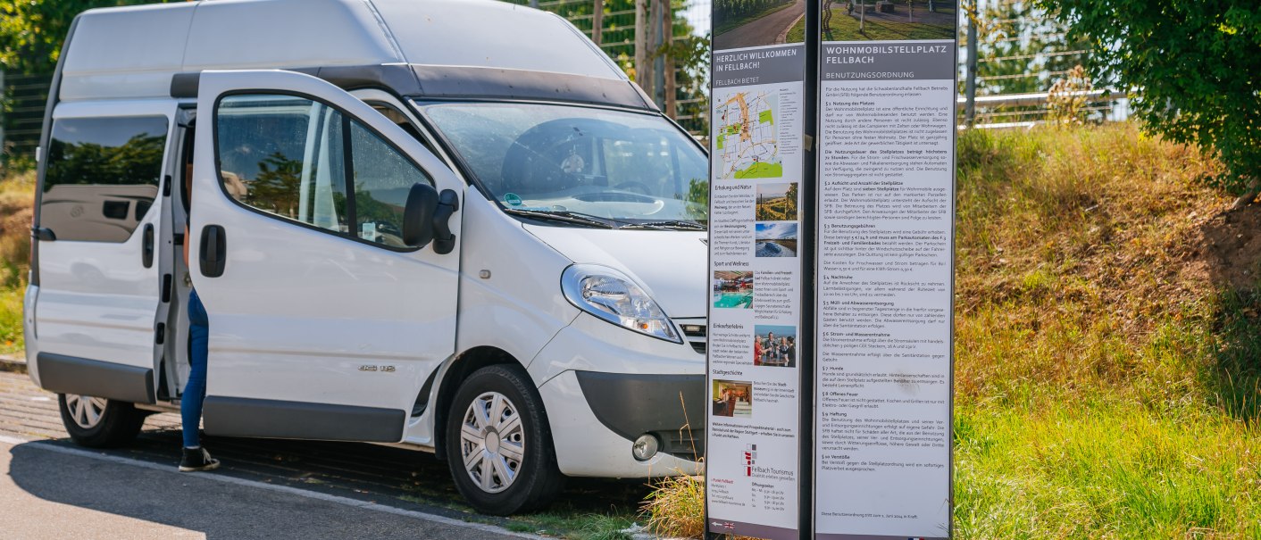 Ein weißer Van parkt neben einer Infotafel auf einem Wohnmobilstellplatz in Fellbach. Eine Person steht halb im Fahrzeug. Sonniges Wetter, grüne Umgebung., © Stuttgart-Marketing GmbH, Thomas Niedermüller Ein weißer Van parkt neben einer Infotafel auf einem Wohnmobilstellplatz in Fellbach. Eine Person steht halb im Fahrzeug. Sonniges Wetter, grüne Umgebung., © Stuttgart-Marketing GmbH, Thomas Niedermüller