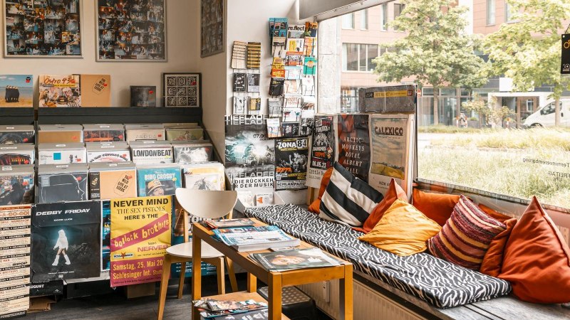 Ein Plattenladen mit Vinyls, Postern und einer gemütlichen Sitzecke mit Kissen. Große Fensterfront mit Blick nach draußen., © SMG, Sarah Schmid