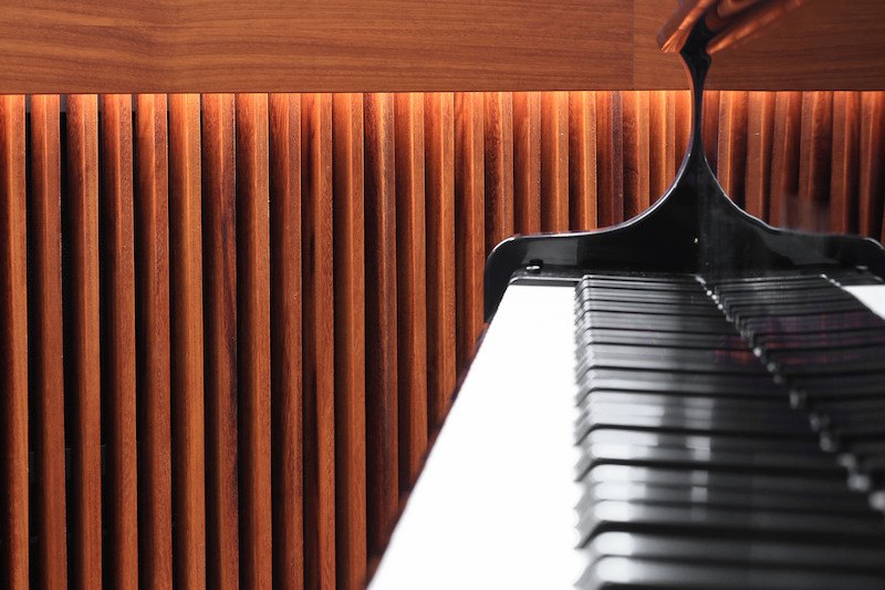 Ein Klavier steht vor einer h&ouml;lzernen Wand mit vertikalen Streben, die von warmem Licht beleuchtet werden., &copy; Literaturhaus Stuttgart