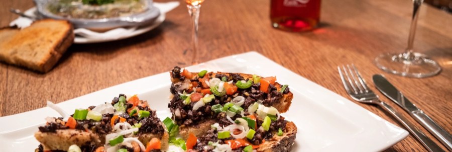 Bruschetta with olive paste and vegetables on a white plate, next to a glass of rosé wine on a wooden table., © Weingut Zaiß
