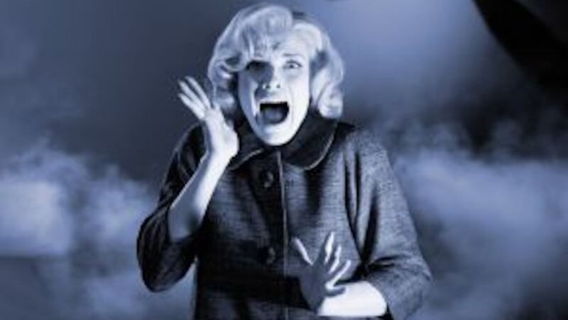 Eine Frau schreit erschrocken, w&auml;hrend der Schatten einer Person mit Messer im Hintergrund sichtbar ist. Die Szene ist in blauem Licht gehalten., &copy; Altes Schauspielhaus und Kom&ouml;die im Marquardt e.V.