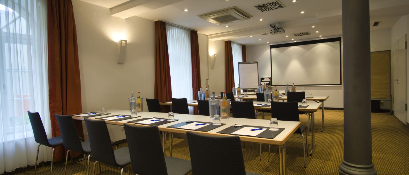 A bright meeting room with tables, chairs, writing materials, water bottles and a screen. The room is prepared for a presentation., &copy; TOMAS