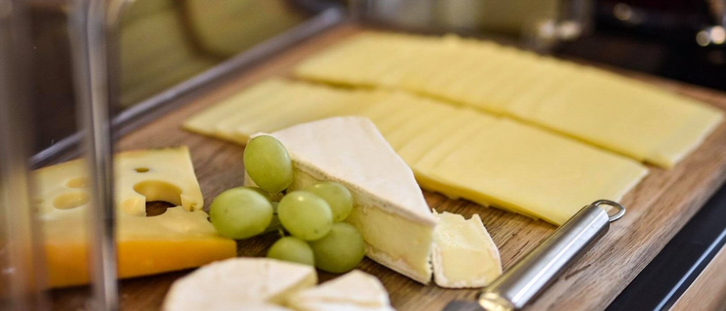 Verschiedene Käsesorten, darunter Brie und Emmentaler, mit grünen Trauben auf einem Holzbrett angerichtet., © TOMAS Verschiedene Käsesorten, darunter Brie und Emmentaler, mit grünen Trauben auf einem Holzbrett angerichtet., © TOMAS