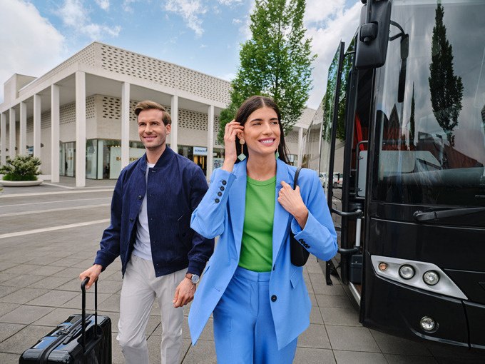 Two people get off a bus in front of a modern building. They look cheerful and are wearing fashionable clothes., &copy; Schlienz-Tours GmbH & Co.KG