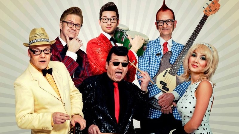 Sechs Personen in bunter, retro-inspirierter Kleidung posieren mit Musikinstrumenten vor einem strahlenförmigen Hintergrund., © C2 Concerts GmbH Sechs Personen in bunter, retro-inspirierter Kleidung posieren mit Musikinstrumenten vor einem strahlenförmigen Hintergrund., © C2 Concerts GmbH