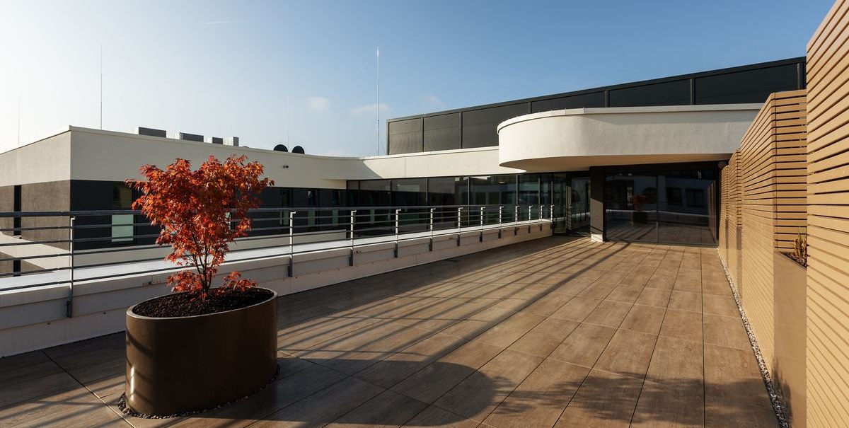 Moderne Terrasse mit Holzfliesen, Geländer und einem kleinen Baum in einem Pflanzkübel. Klare Linien und minimalistisches Design., © Novum Hospitality