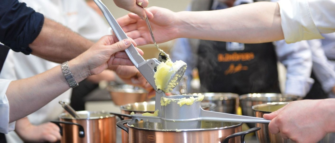 Several people use a potato ricer to press potatoes into a pot. More pots can be seen in the background., © Ilzhöfer, Stuttgart Several people use a potato ricer to press potatoes into a pot. More pots can be seen in the background., © Ilzhöfer, Stuttgart