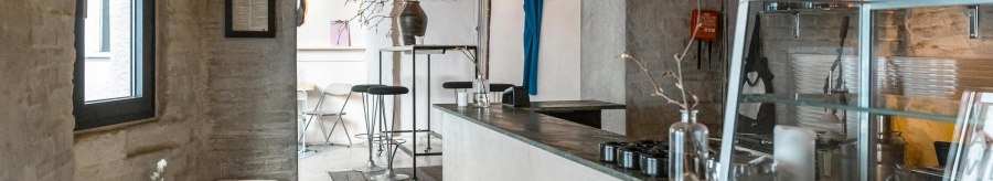 Modern café with minimalist décor, white walls and wooden furniture. A blue piece of clothing hangs on the wall, plants on tables., © SMG Stuttgart Marketing GmbH - Sarah Schmid