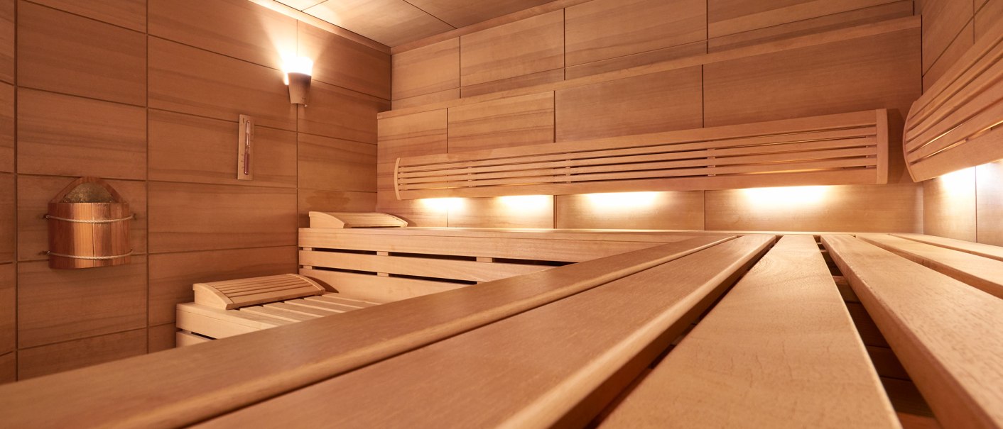 Moderne Sauna mit Holzbänken, sanfter Beleuchtung und einem Eimer an der Wand. Die Wände und Decke sind aus hellem Holz., © TOMAS Moderne Sauna mit Holzbänken, sanfter Beleuchtung und einem Eimer an der Wand. Die Wände und Decke sind aus hellem Holz., © TOMAS