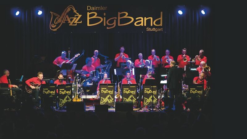 Die Daimler Jazz Big Band spielt auf einer Bühne in Stuttgart. Musiker in roten Hemden, Instrumente und Notenständer sind zu sehen., © Rosenau Kultur e.V.