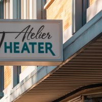 Ein Schild mit der Aufschrift 'Atelier Theater' hängt an einem Gebäude. Die Fassade ist modern und das Wetter ist sonnig., © SMG, Sarah Schmid Ein Schild mit der Aufschrift 'Atelier Theater' hängt an einem Gebäude. Die Fassade ist modern und das Wetter ist sonnig., © SMG, Sarah Schmid