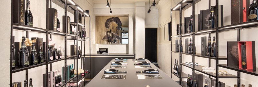 Moderner Weinladen mit eleganten Regalen, gefüllt mit Kessler-Flaschen und Verpackungen. Ein stilvolles Ambiente mit zentralem Tisch und Beleuchtung., © KESSLER Sekt GmbH & Co. KG