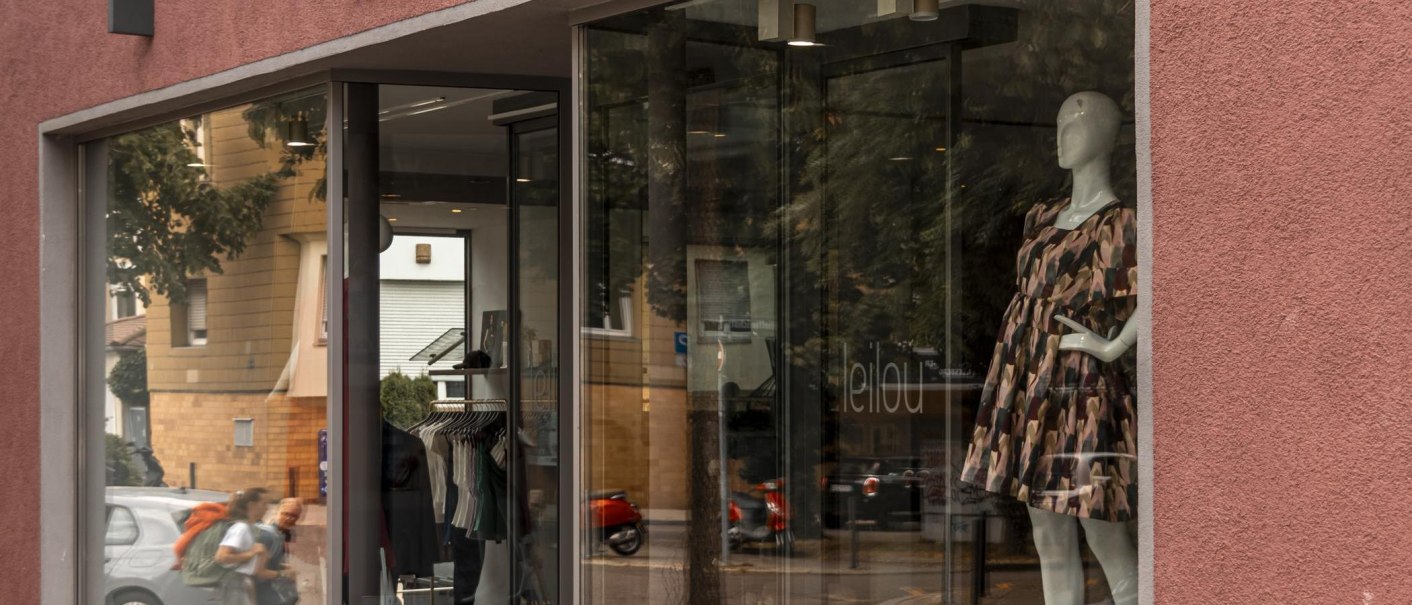Shop window of a clothing store with a mannequin in a patterned dress. Trees and a building can be seen in the background., © SMG Stuttgart Marketing GmbH - Sarah Schmid Shop window of a clothing store with a mannequin in a patterned dress. Trees and a building can be seen in the background., © SMG Stuttgart Marketing GmbH - Sarah Schmid
