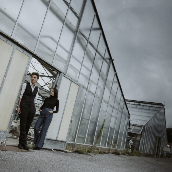 Zwei Personen stehen vor einem gro&szlig;en Gew&auml;chshaus. Der Himmel ist bew&ouml;lkt, und die Szene wirkt leicht melancholisch., &copy; Veranstalter