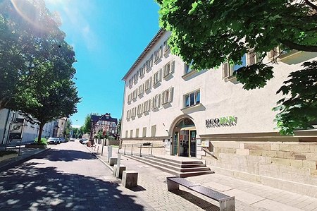 A building labeled 'BQQ INN' on a sunny street, surrounded by trees and clear skies., &copy; ECOINN Hotel am Campus