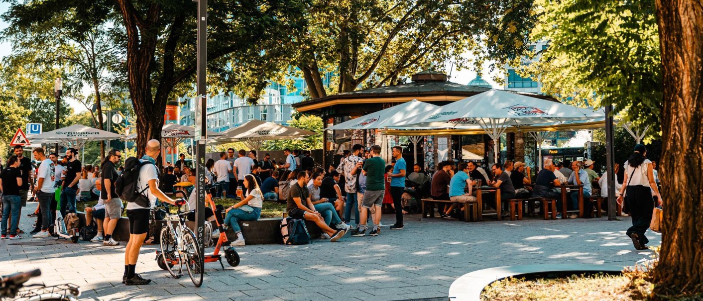 Belebter Biergarten mit vielen Menschen unter Sonnenschirmen, umgeben von Bäumen. Einige sitzen, andere stehen und unterhalten sich., © Stuttgart Marketing GmbH, Sarah Schmid