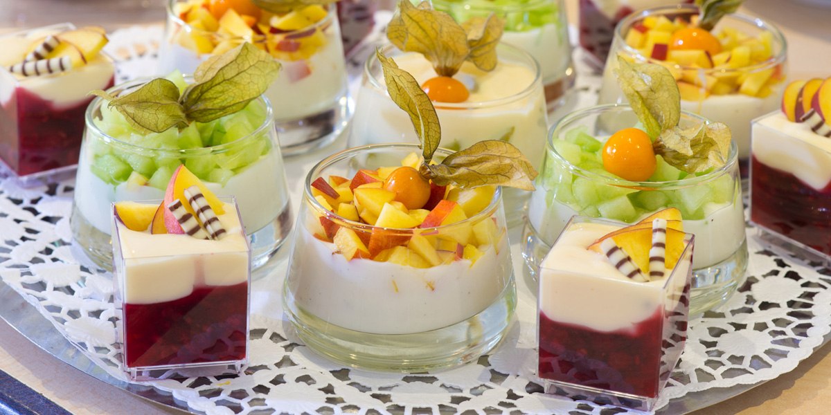 Various dessert glasses filled with yogurt, fresh fruit, and physalis, arranged on a decorative tray., &copy; ACHAT Hotels Deutschland